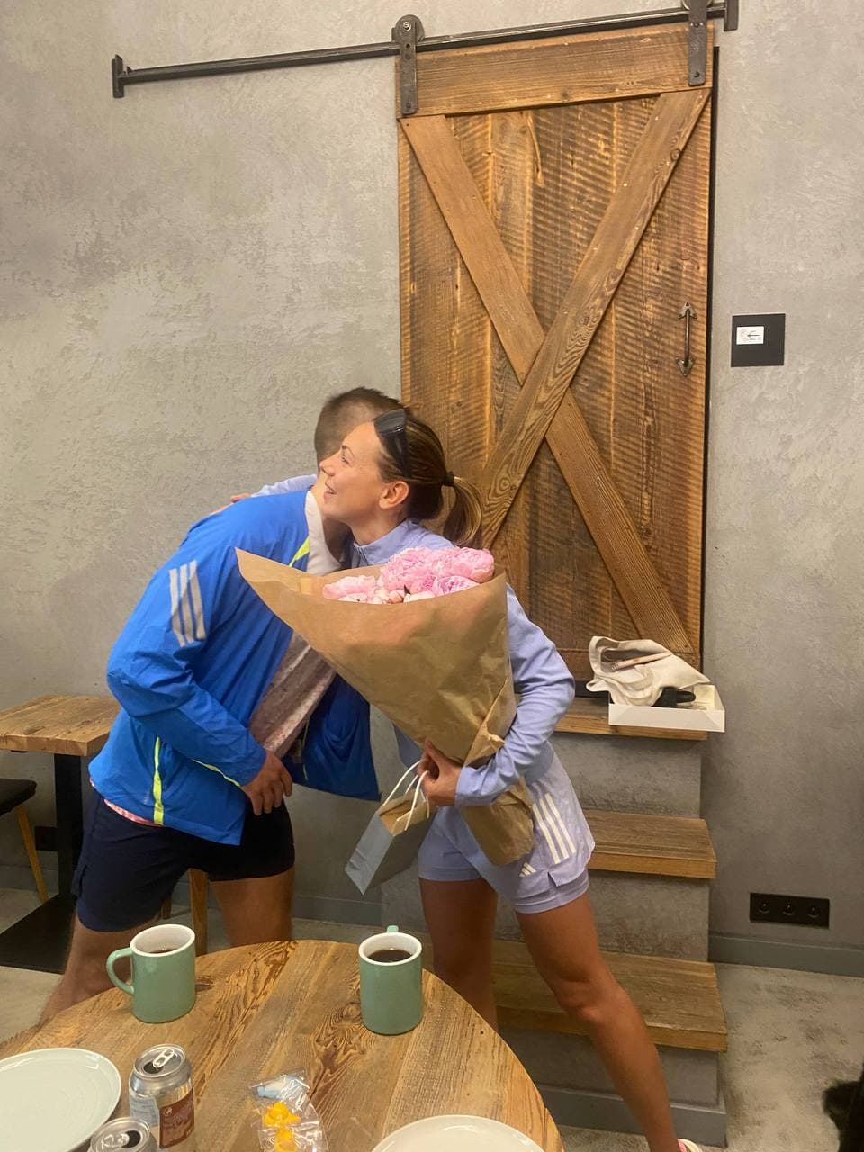 A runner receiving a bouquet of flowers and a hug indoors